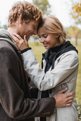 Fototapeta premium joyful young couple with closed eyes embracing in autumnal park during date.
