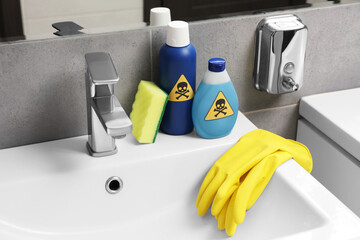 Bottles of toxic household chemicals with warning signs, gloves and scouring sponge in bathroom