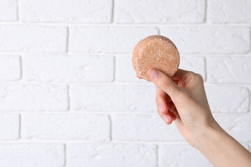 Woman holding solid shampoo bar against brick white wall, closeup. Space for text