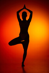 Silhouette of female full-length body isolated over orange background. Standing on yoga pose