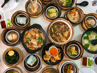 Flat lay of assorted traditional Chinese dim sum in bamboo steamer with a variety of appetitzers freshly served on table