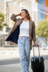 happy young travel woman pulling suitcase on city street