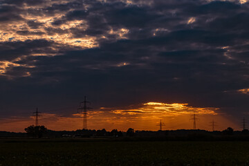 Beautiful sunset with a dramatic sky and overland high voltage lines near Tabertshausen, Bavaria, Germany