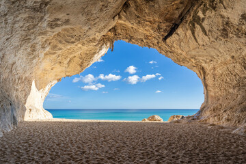 View of a calm blue sea from inside a cloud-shaped cave on a beach
