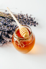 close-up on a jar of honey and a wooden spoon for honey with lavender flowers on a white background