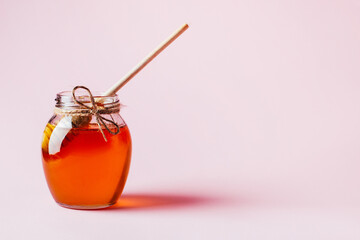 close-up on a jar of honey and a wooden spindle for honey on a pink background