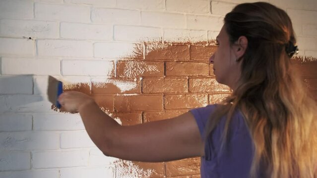 girl paints a brick white wall in brown, coffee color , brush stirs paint
