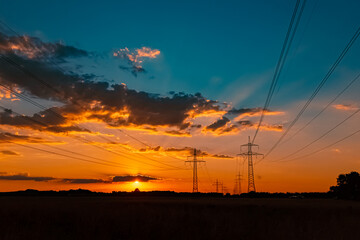 Naklejka na ściany i meble Beautiful sunset with a dramatic sky and overland high voltage lines near Tabertshausen, Bavaria, Germany