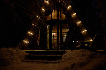 Wooden house chalet cottage covered with snow in winter with the lights on.
