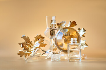 Biophilic Autumn background. Gilded gold oak leaves distorted by transparent glass jars, small bottles. Monocholored orange beige earth colored floral elements with reflections on matching background.