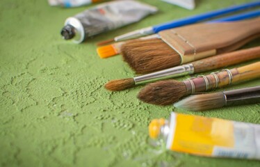 Obraz premium Artistic brushes and watercolor paints on a green textured background. Hobbies and creativity for children and adults. Selective focus.