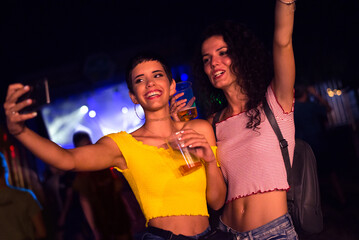 Two happy young girls dancing and drinking beer on the party concert in the night club	