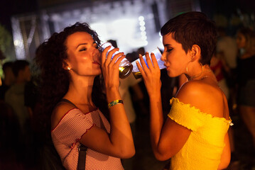 Two happy young girls dancing and drinking beer on the party concert in the night club	