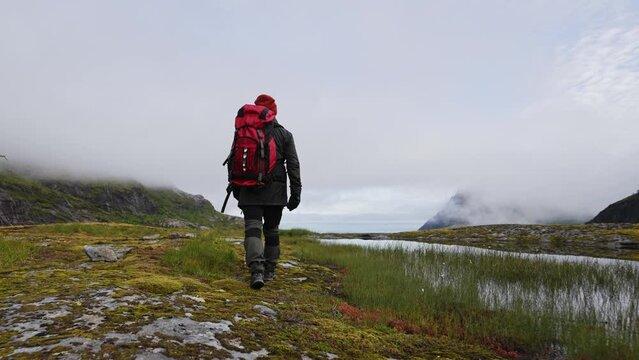Solo traveler with a big red backpack walks along the tops of the mountains Norway near Munken and Munkebu.