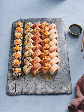 Close up view of beautifully plated gunkan and maki sushi set on stone serving board on dark background