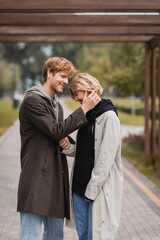 happy young man in autumnal coat hugging woman under arch in park.