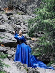 A beautiful woman in a long blue dress, black leather corset and black lace gloves surrounded by rocks. Forest Nymph. Full length portrait.