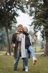 Fototapeta premium full length of happy redhead man and pleased young woman holding coffee to go while walking in park.