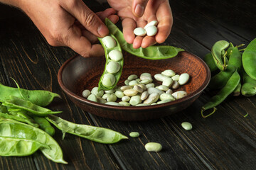 Cleaning bean seeds from green pods by the hands of a cook after harvesting. Work environment on the kitchen table.