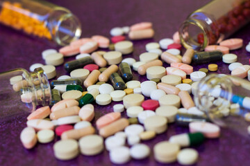 Medical bottles and medication pills spilling out on to purple background