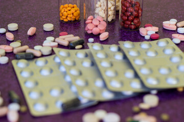 Medical bottles and medication pills spilling out on to purple background