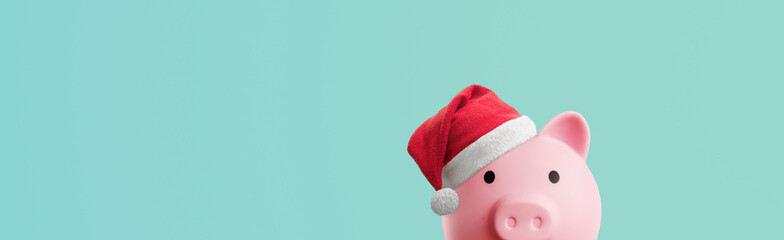 Pink piggy bank with santa claus hat on a blue background - saving concept for christmas