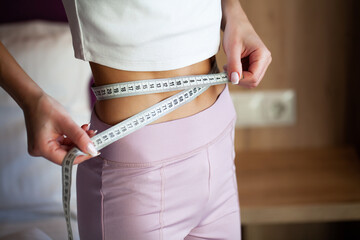 Slim woman measuring her waist with a measure.