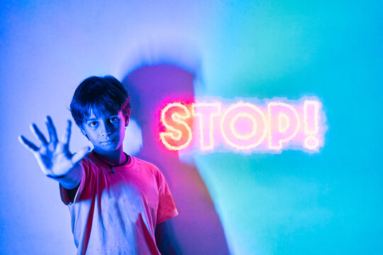 Serious boy near neon stop inscription