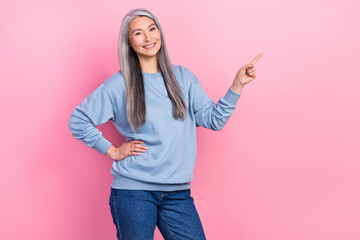 Photo of cute shiny retired woman blue sweater pointing empty space isolated pink color background