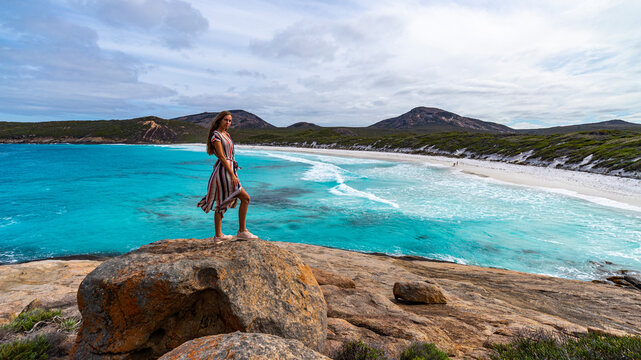 girl in long dress stands on rocks admiring the power of the ocean; amazing beach with turquoise water, hellfire bay near esperance in western australia