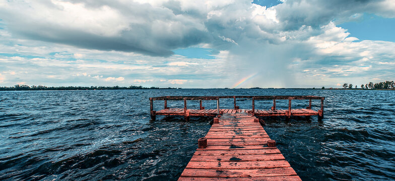 wooden pier on blue lake with rainbow in the sky