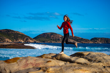 beautiful long-haired girl jumps over rocks by the ocean; girl captured while jumping in motion;...