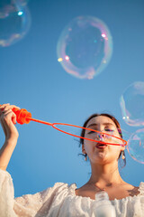The girl blows soap bubbles against the blue sky.