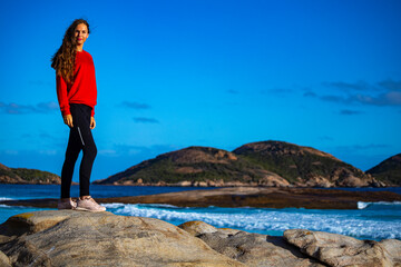 beautiful long-haired girl stands on the rocks above the ocean admiring the sunset; sunset on lucky bay beach in western australia