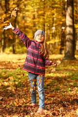 Sunlit portrait of a cheerful girl throwing leaves in the autumn park