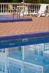 The hotel's terrace with children's and adult swimming pools. The building is reflected in the light blue water of one of the pools. Selective focus.