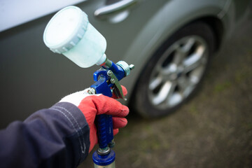 A gloved hand with a paint gun. Painting the car. Selection of paint for the car.