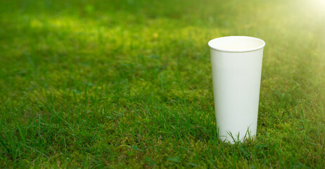 A white cup of coffee on the green grass. A clean white cup with a place for text. Sale of drinks.