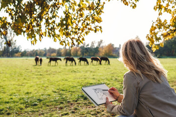 Woman artist sketching horse in autumn outdoors. Pencil drawing