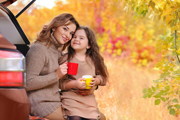 Smiling mother and daughter drinking tea in the car trunk