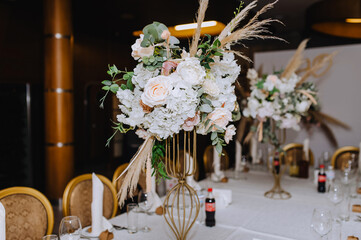 Flowers, reeds, wild flowers stand in a metal vase on a table in a restaurant, as a decoration.