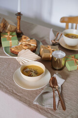 Pumpkin soup, apple pie, candles, gifts on linen tablecloth. Cozy home atmosphere.  Aesthetic family dinner.