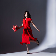 Full length photo of beautiful woman posing in a red dress holding a bouquet of tulips, posing to the camera.