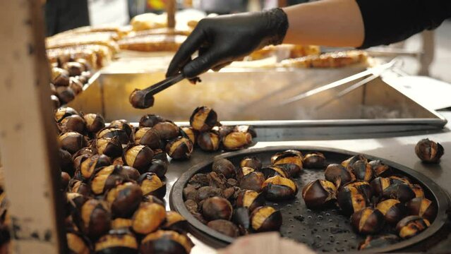 Close up: Delicious Chestnut grilling over glowing coals, make street food in Istanbul, Taksim square. Barbecued roasted on hot stove fresh tasty chestnut, male hand flips 