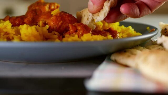 Dipping naan bread into chicken Korma curry with Pilau rice 