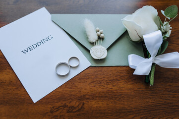 Wedding details and accessories close-up: rose boutonniere, gold rings, an envelope with a seal...