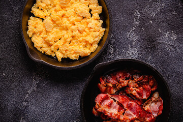 Cooked scrambled eggs and fried bacon in portion pans