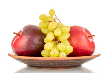 Two red apples and grapes on a clay plate, macro, isolated on white background.