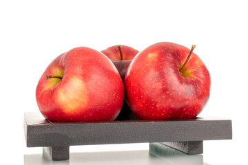 Still life of three red apples on a black wooden plate, macro, isolated on white background.