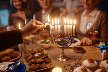 Close up of father lighting candles in menorah while celebrating Hanukkah with his extended family.